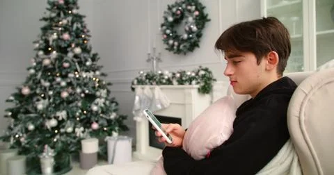 Young man browsing phone on sofa, Christmas tree in background Stock Photos