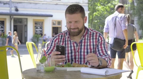 Young man browsing smartphone, during lunch, slider and pan shot. Vidéo 67604096