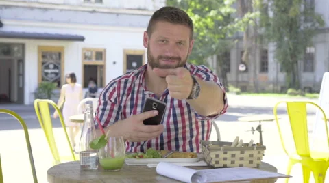 Young man browsing smartphone during lunch, points the finger camera. Vidéo 67604222