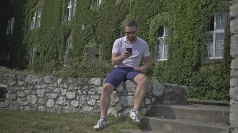 Young man browsing smartphone, sitting on the wall. 库存影片 65521991