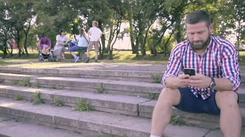 Young man browsing smartphone, sitting on stairs in park. Slider shot. Vidéo 67240524