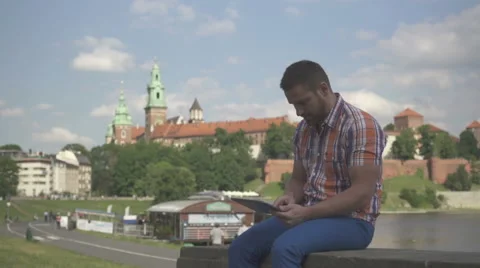Young man browsing tablet sitting on wall. Vídeo Stock 52696214