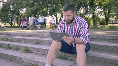 Young man browsing tablet, sitting on stairs. Slider shot. 库存影片 67241943