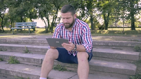Young man browsing tablet, sitting on stairs. Slider and pan shot. Vidéo 67242217
