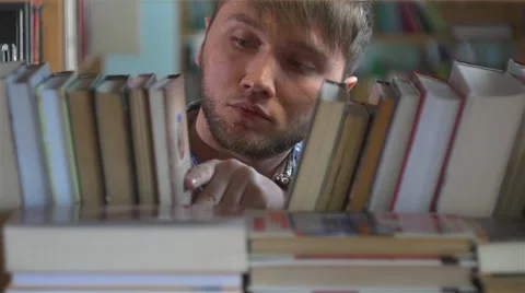 Young man browsing through the racks of books in a library Stock Footage 49896863