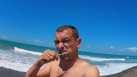 Young man brushes his teeth while standing outside against backdrop of sea. Stock Footage 204993948