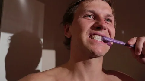 Young man brushing his teeth. He is standing topless in the bathroom. Stock Footage 76117352