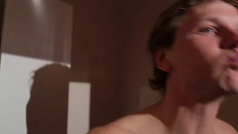 Young man brushing his teeth. He is standing topless in bathroom. Rinsing mouth. Video stock 76117415