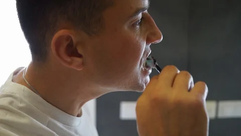 Young Man Brushing Teeth In Bathroom in front of mirror. Doing hygiene routine Stock Footage 121003222