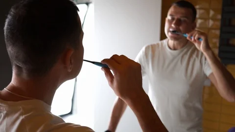 Young Man Brushing Teeth In Bathroom in front of mirror. Doing hygiene routine Stock Footage 124308258