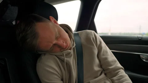 Young man, buckled up, sleeps in the back seat of a car during a trip. Stock Footage 280386776