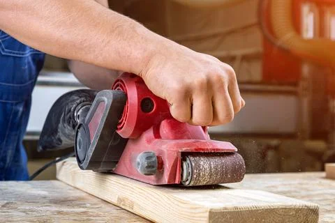 Young man builder carpenter equals polishes wooden board with a  random orbit Stock Photos
