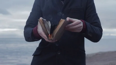 Young man with burning book in hand standing on coast storm clouds on background Stock Footage 74363722