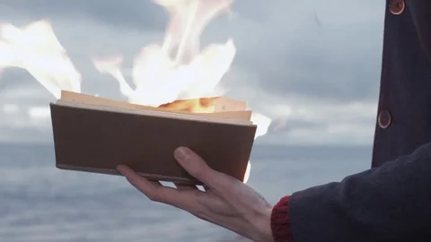 Young man with burning book in hand standing on coast storm clouds on background Stock Footage 74363803