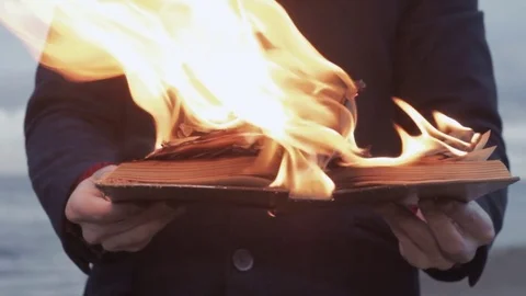 Young man with burning book in hand standing on coast storm clouds on background Stock Footage 74363893