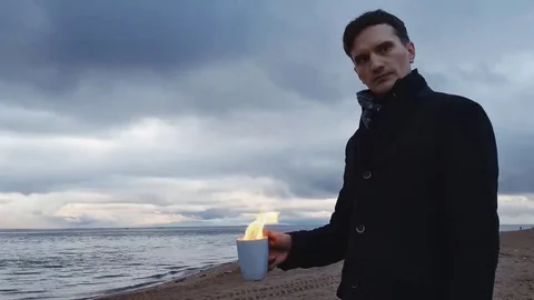 Young man with a burning cup in hand standing on coast storm clouds on Stock Footage 69149418