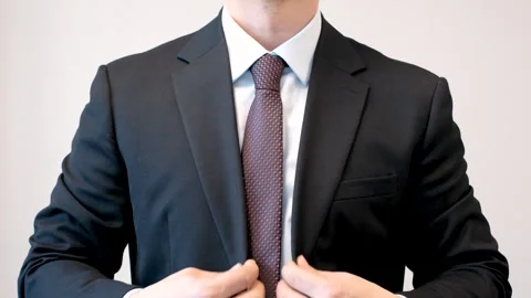 Young man in business suit adjusting jacket front view on gray background. Stock Footage 303385952