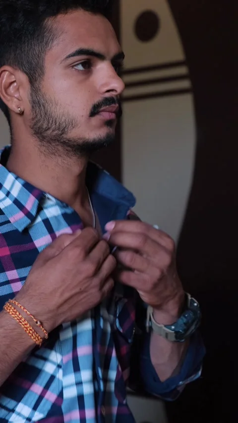 Young man buttoning up his plaid shirt, getting ready for the day Видео 331354532