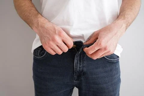 Young man buttoning jeans on a gray background, close-up. Foto stock