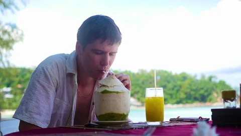 A young man in a cafe drinking a cocktail on terrace. outdoors. Coconut water Vidéo 75996788