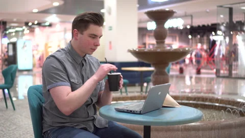 Young man in a cafe with a laptop on the background of a fountain. Decoration in Stockbeeldmateriaal 152487425