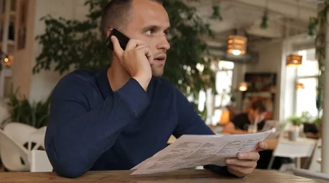 Young man in cafe or restaurant, looking through the menu talking phone Stock Footage 67862176