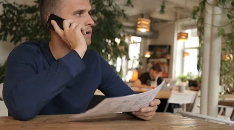 Young man in cafe or restaurant, looking through the menu talking phone Stock Footage 67862223