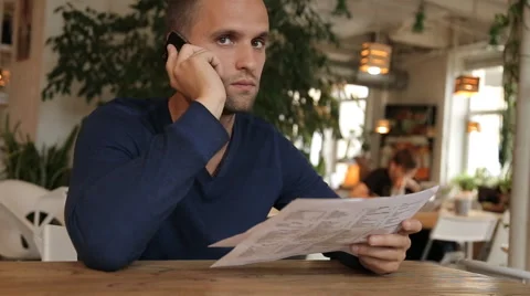 Young man in cafe or restaurant, looking through the menu talking phone Stock Footage 67862263