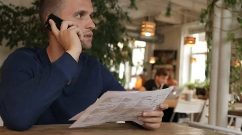 Young man in cafe or restaurant, looking through the menu talking phone Stock Footage 67862308