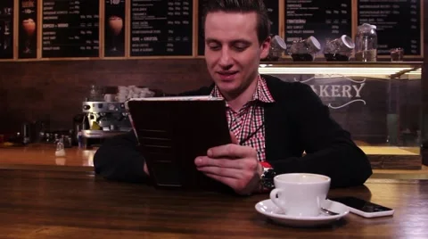 A young man in a cafe, sitting at the table with tablet PC, typing something 스톡 동영상 49766615