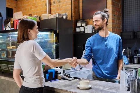 Young man cafe worker shaking hands with woman client customer colleague in Stock Photos