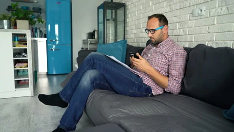 Young man calculating bills on smartphone sitting on sofa Vídeo Stock 89550683