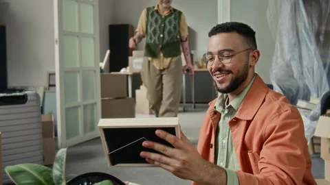 Young Man Calling to Girlfriend and Showing Framed Picture when Unpacking Box Stock Footage 323304644