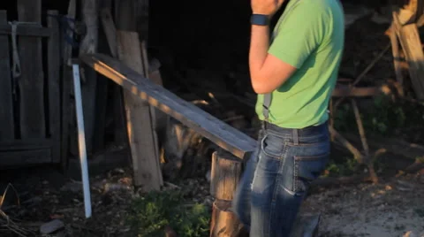 Young man calling by phone at sunset. A man sits at the sawmill Stock Footage 64776389