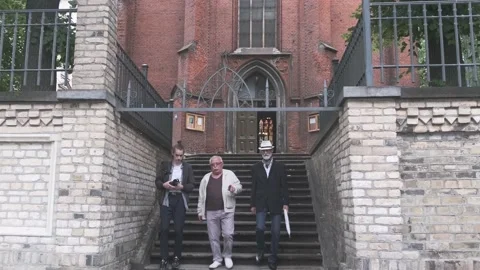 Young man with camera and senior men go down steps by church Stock Footage 139796016