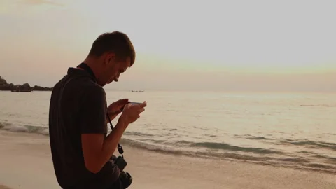 Young man with a camera stands on the beach and shoots video on a smartphone Stock Footage 146072131