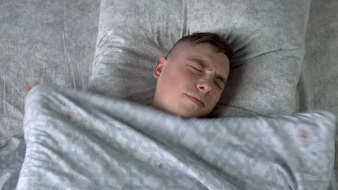 A young man cannot fall asleep. A man lies in bed in his room and suffers from Stock Footage 128015471
