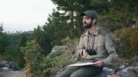 Young man with cap and uniform holds binoculars and a map and looks into the Stock Footage 241738330