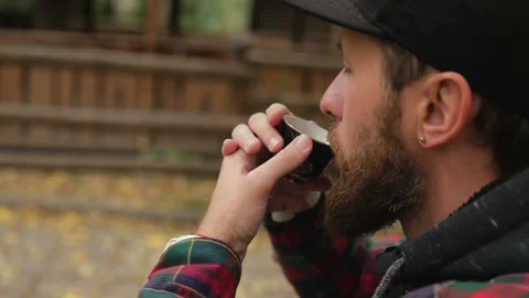 A young man in a cap with a beard drinks Chinese tea from a bowl. outdoor Stock Footage 220415331