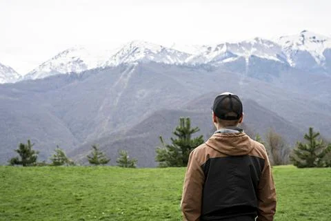 Young man in cap from behind looking view of snow capped peak mountain ridge Foto stock