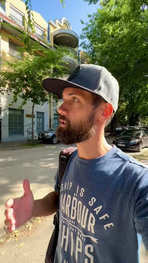 A young man in a cap films himself and tells a story as he walks through a city  Stock Footage 252086504
