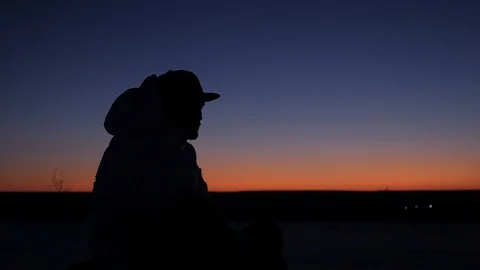 A young man in a cap sits thoughtfully at sunset and dreams Stock Footage 104057508