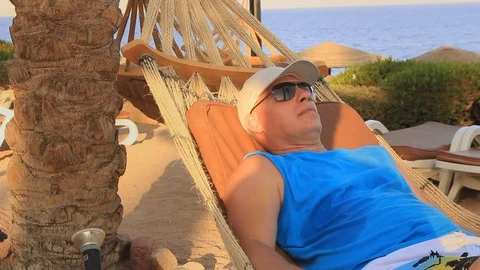 A young man in a cap from the sun is resting in a hammock on the seashore on a s Stock Footage 116050605