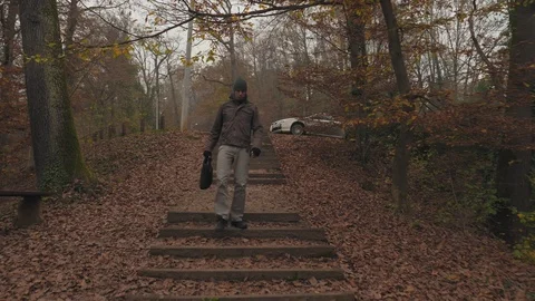 Young man with cap walking down the stairs in the forest park in autumn Video stock 98111433