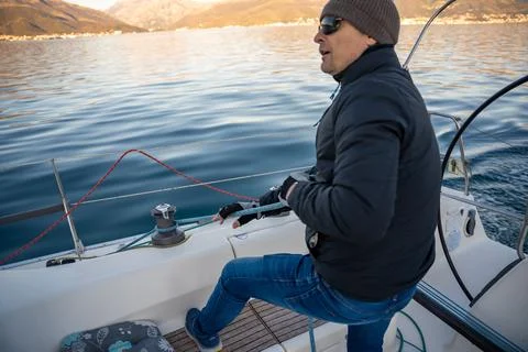 Young man captain operates and controls a sailboat during a journey by sea in Stock Photos