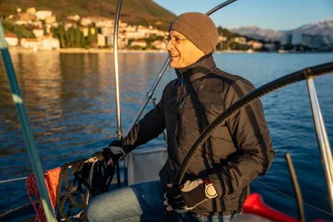 Young man captain standing at the helm and controls a sailboat during a journey Stock Photos