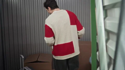 Young Man Carrying Cardboard Box and Loading It into Storage Unit Stock Footage 327779244