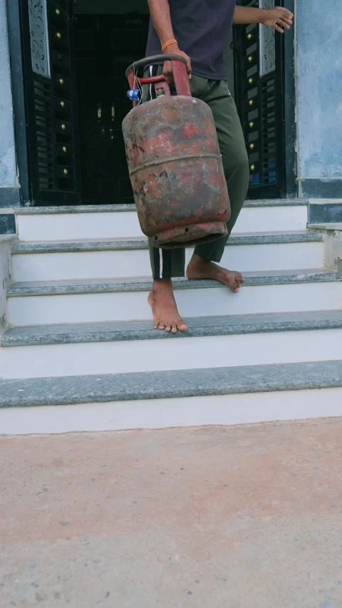 A young man carrying a heavy rusty LPG gas cylinder down the stairs 스톡 동영상 333058030