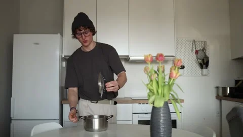 A young man in casual clothes opens a pot in a modern kitchen, preparing to cook Video stock 302635149