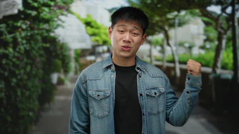 Young man in casual denim jacket gesturing while standing in a tranquil par.. Stock Footage 309883828